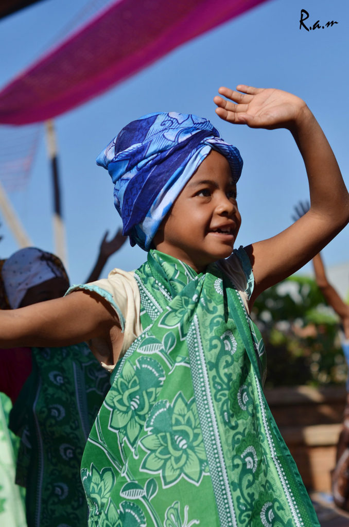junges Mädchen aus dem Bildungszentrum tanzt mit Armen über dem Kopf und einem grünen Tuch um den Schultern sowie einem blauen Turban