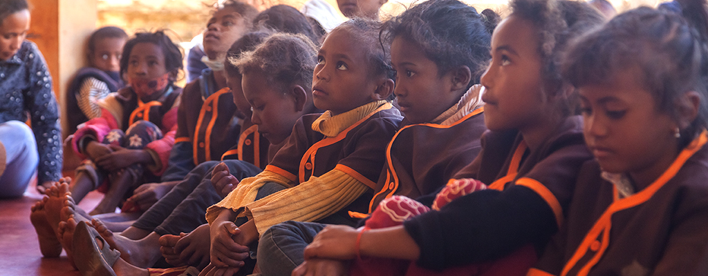madagassische junge Mädchen sitzen in ihrer Schuluniform auf dem Lehmboden im Bildungszentrum und gucken nach vorne